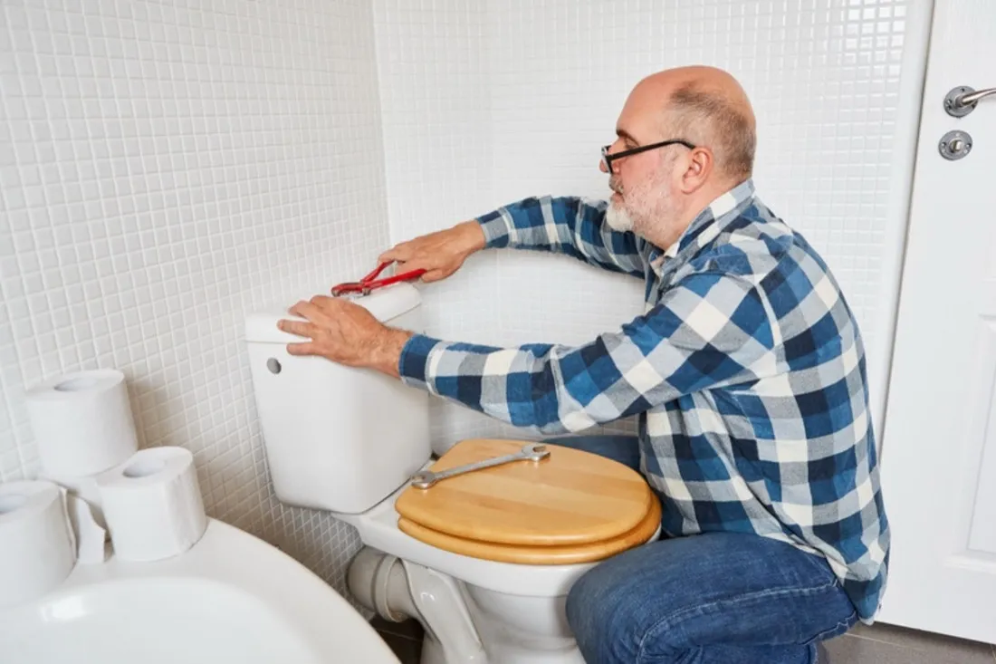 Håndværker sidder ved et toilet og monterer cisternen